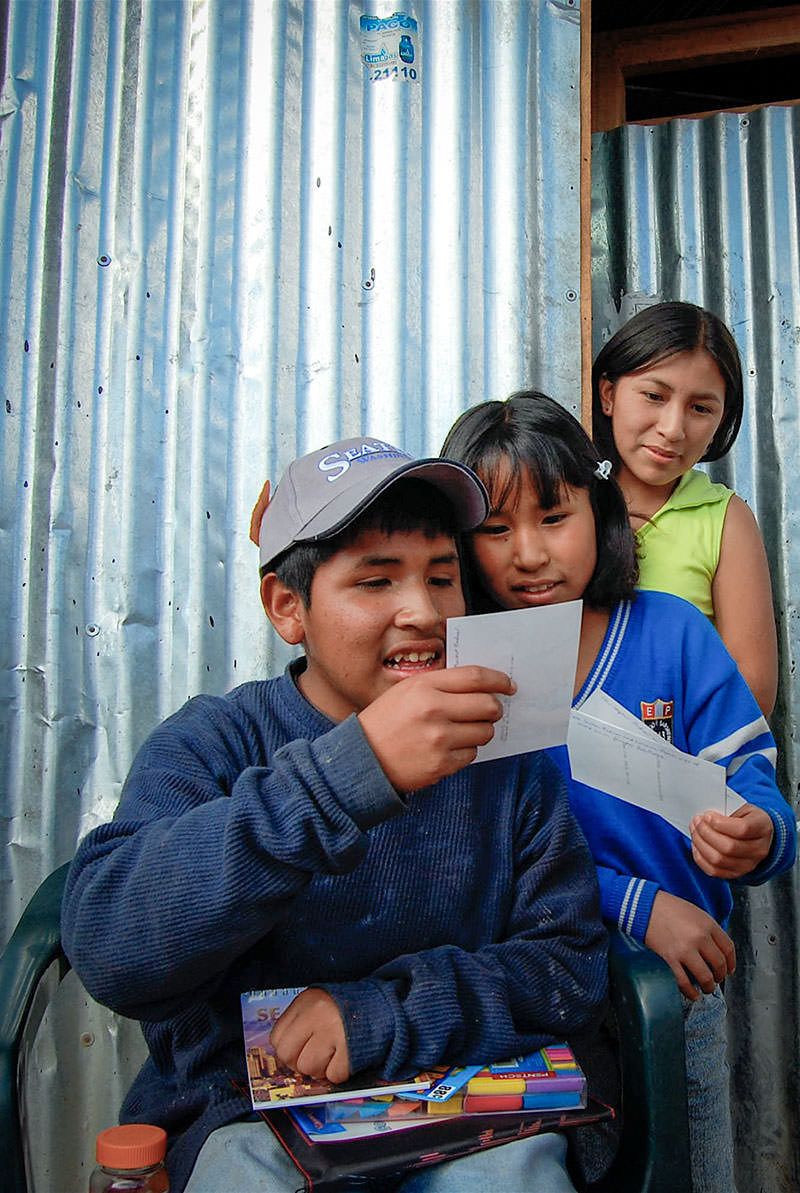 Two of Jhon’s sisters look on while he inspects photos and gifts Jane Sutton-Redner sent with World Vision magazine’s Ryan Smith on a visit to Huanta in 2007.