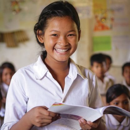 Girl smiles holding her textbook in her classroom