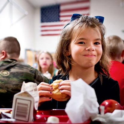 Young girl smiles at the camera in her lunch room at school in the United States.