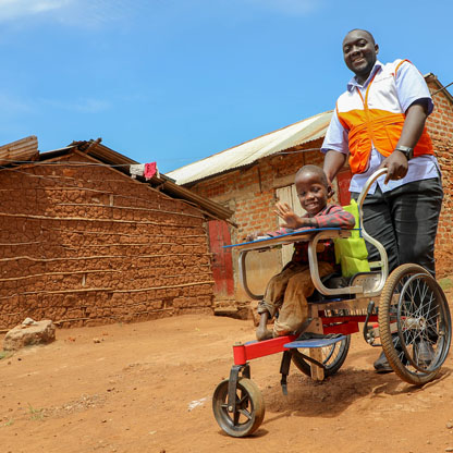 Child in wheelchair smiles and waves with a World Vision employee