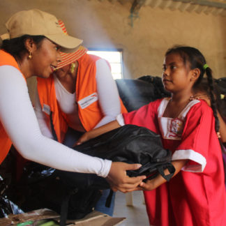 World Vision employee hands backpack with supplies to a young Venezuelan girl
