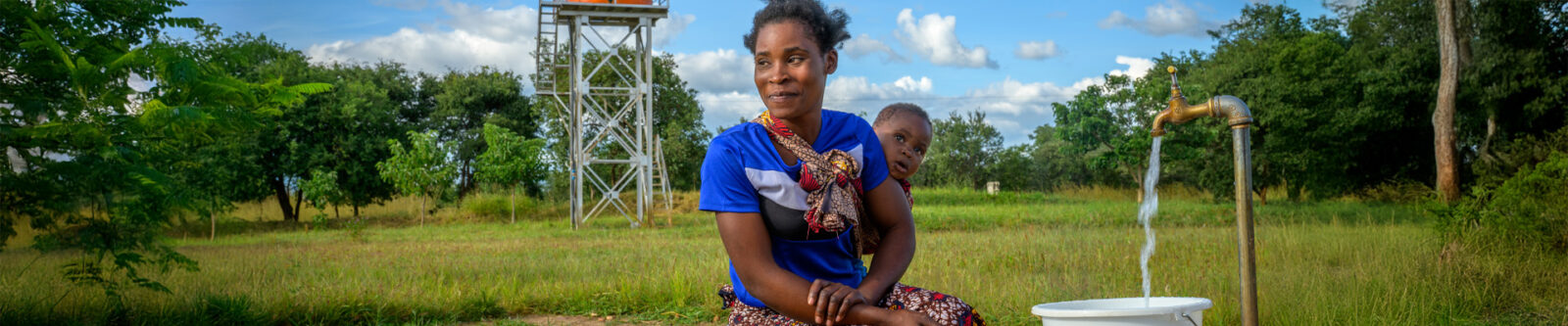 woman holding her baby while getting clean water