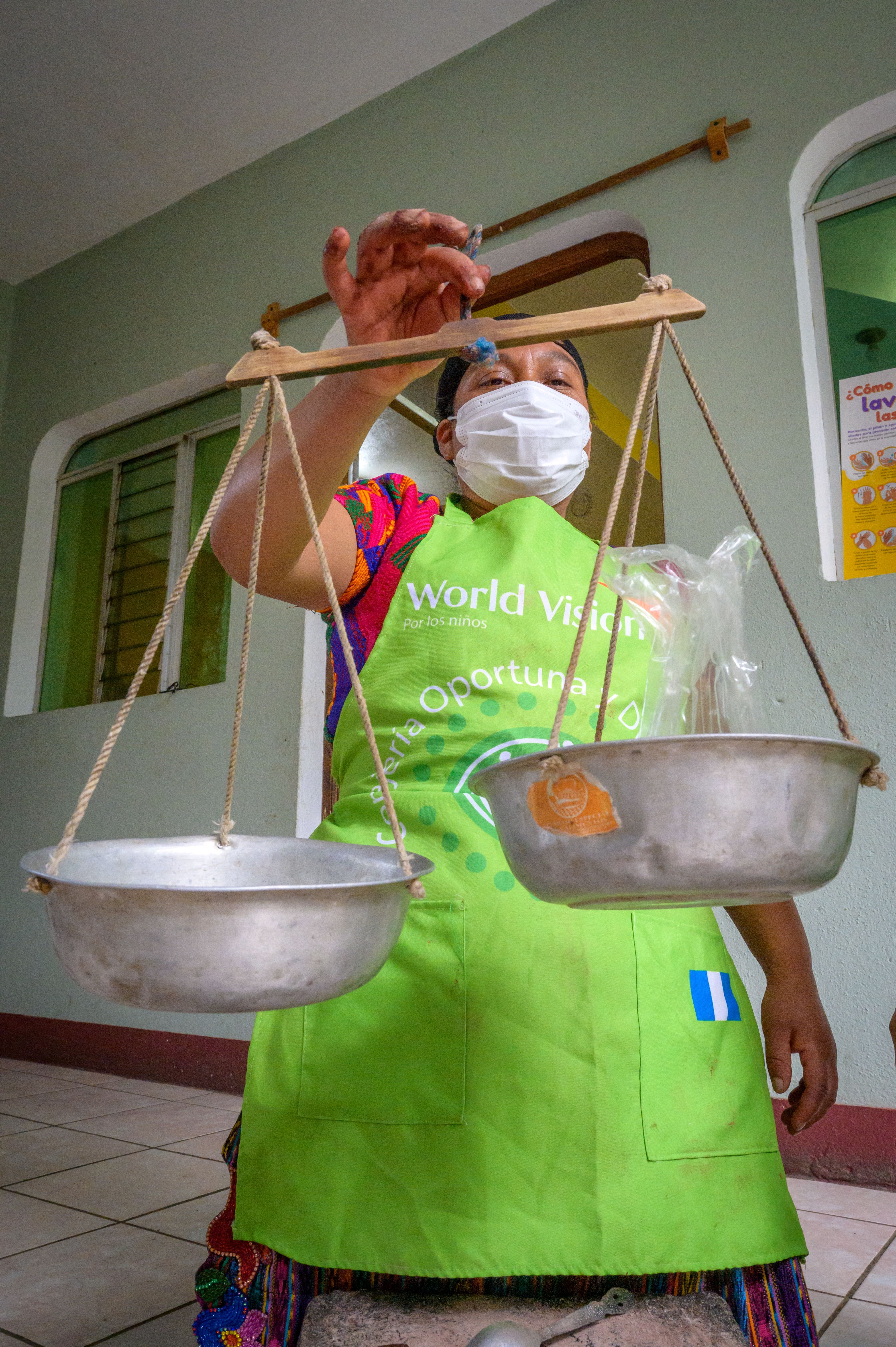 A woman wearing a mask holds uneven scales in front of her.