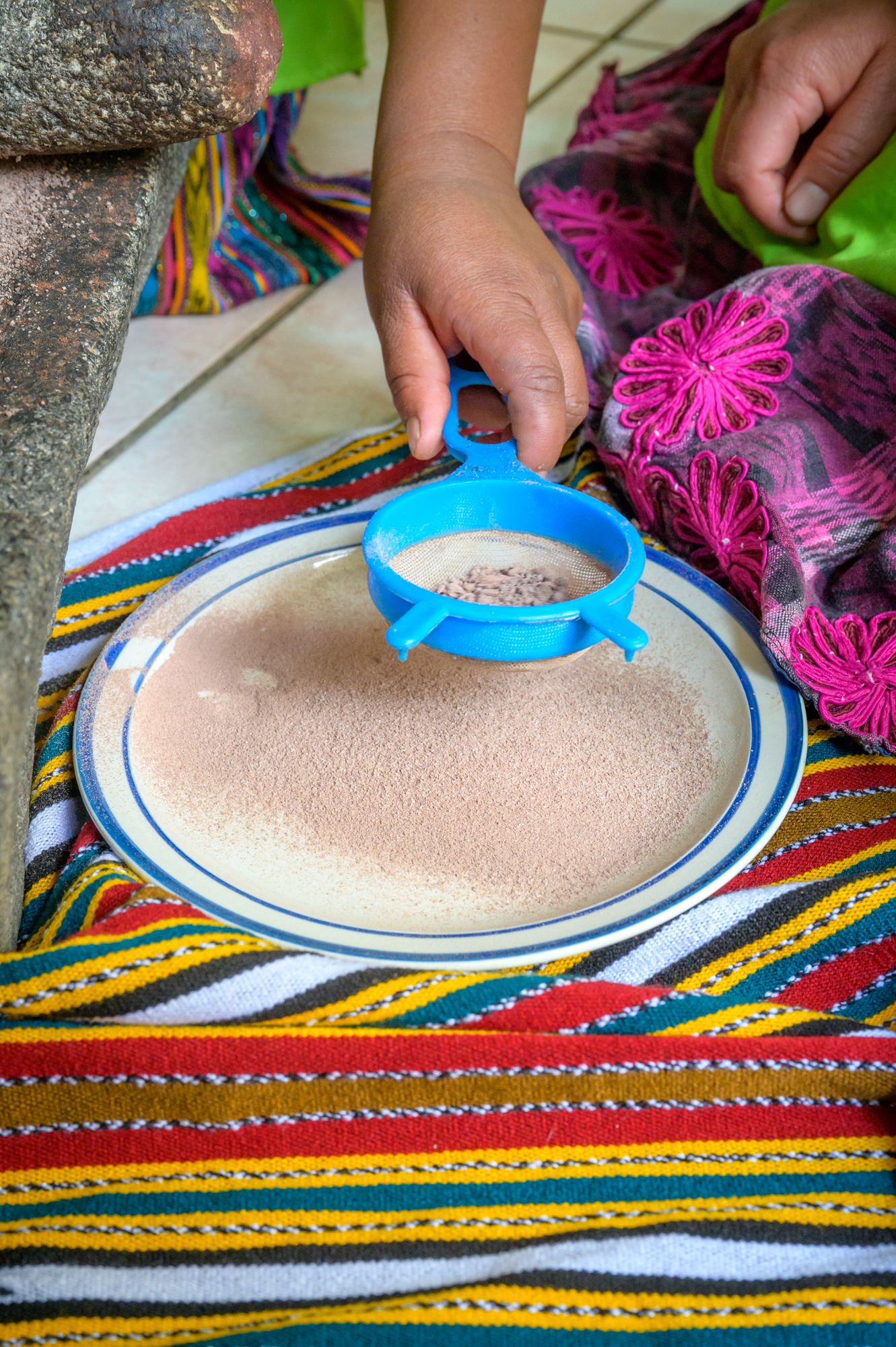 A hand sifts chocolate powder through a sieve onto a plate.
