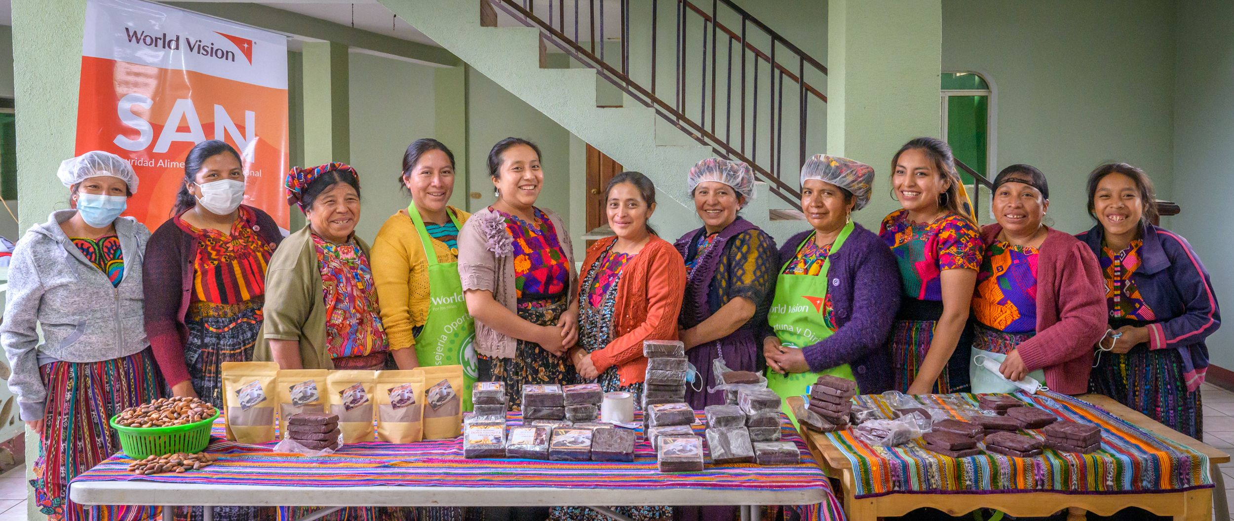 A group of women smile widely as they stand behind a table covered with chocolate products.