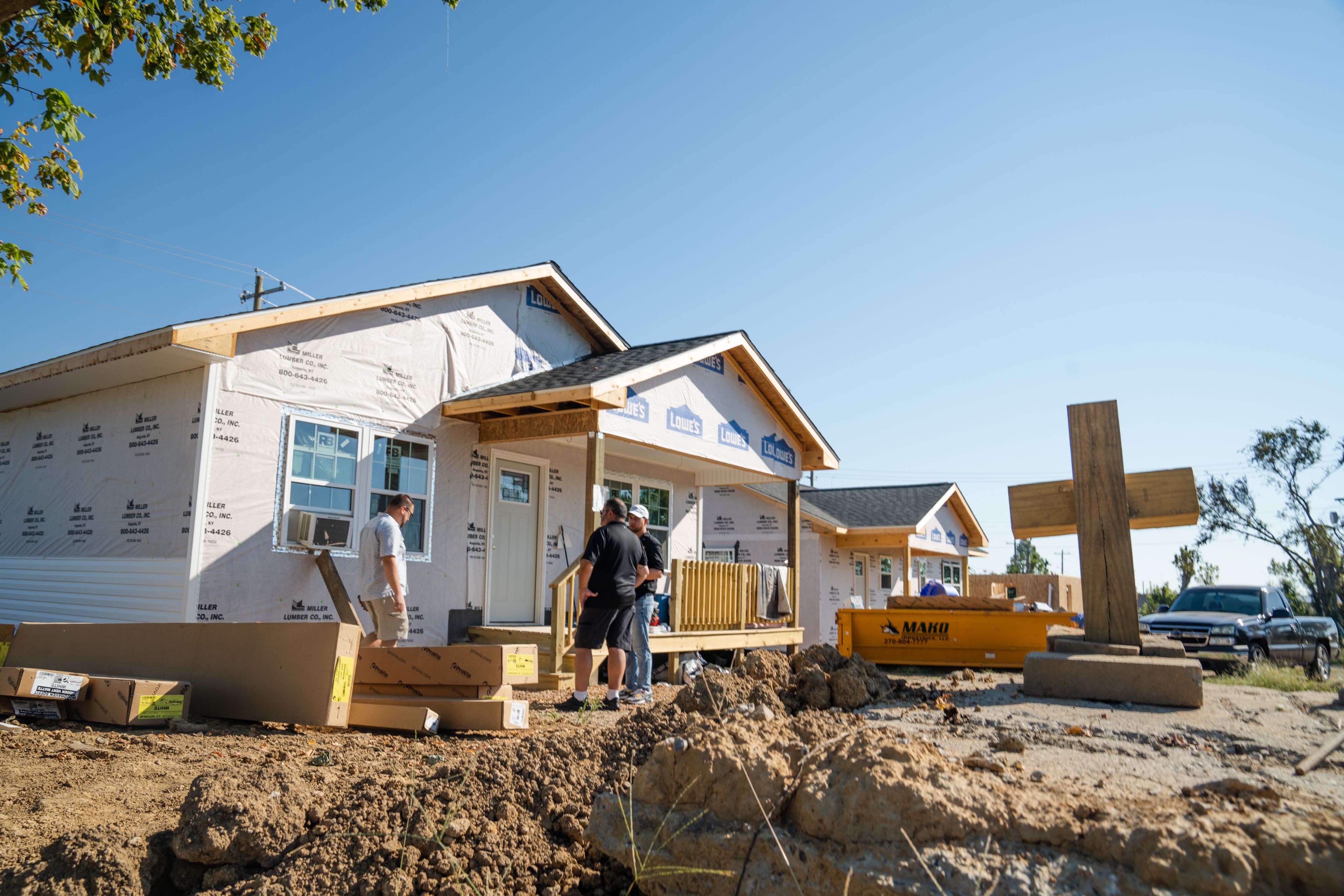 A large wooden cross stands outside of a house under construction. 