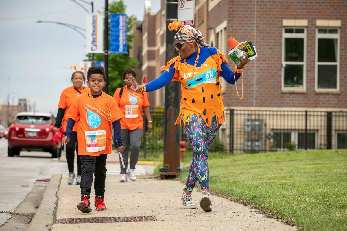 A woman in an orange shirt with a Global 6K bib reaches out to the boy next to her wearing World Vision’s Global 6K shirt. 