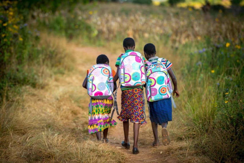Zambian girls walk to school wearing new backpacks from World Vision.