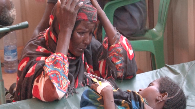 A grandmother in Somalia looks on with worry as her young grandchild is treated for watery diarrhea.