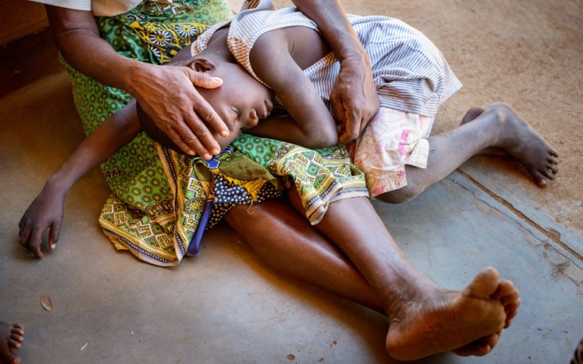 Child with malaria resting head in mother's lap.