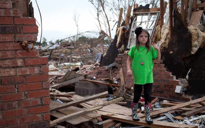 Young girl walking among destroyed home after tornado in Oklahoma.