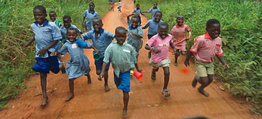 Children running in a group down a dirt road.