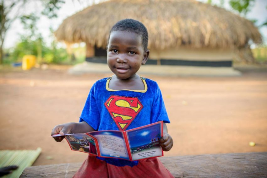 Superheroes. Defin, 3, looks at a Christmas card her brother, Joshua Ogwang, 10, received from his sponsors, who live in California. (©2014 World Vision/photo by Jon Warren)