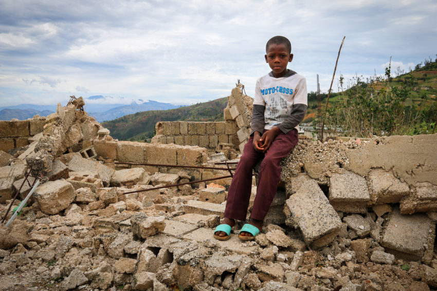 Enivens sits on the crumbled blocks that are all remaining of his family’s home after Hurricane Matthew blew through Haiti. (©2016 World Vision, Santiago Mosquera)