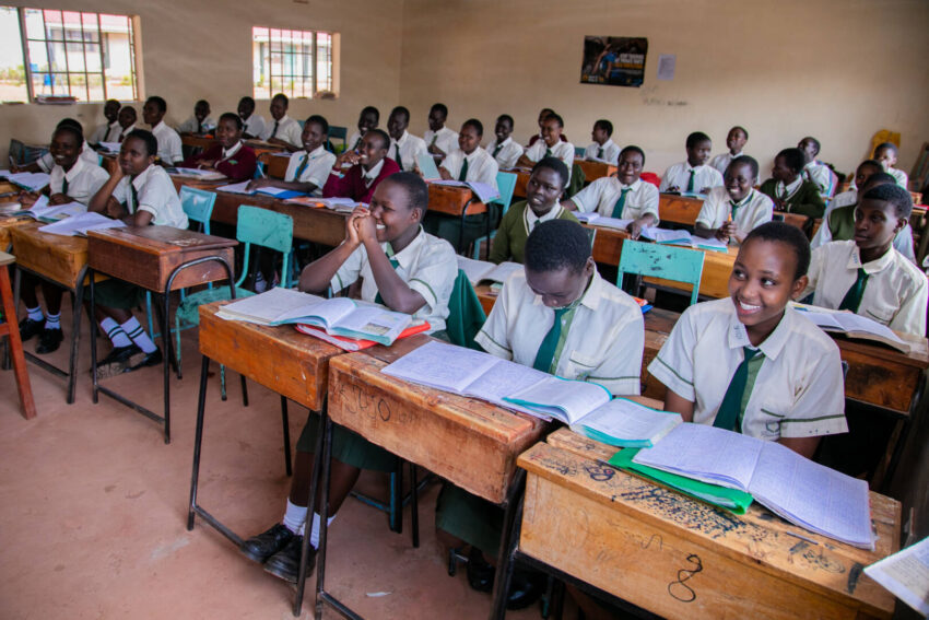 In a full classroom, high school girls wearing white uniforms smile from their desks.