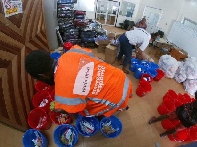 Aid workers bend to sort and organize relief supplies laid out on the floor.