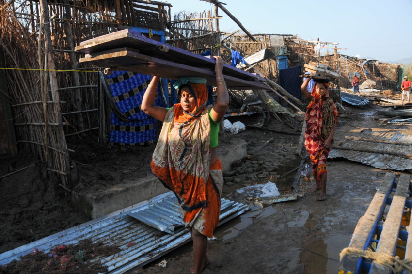 Women carry salvaged building supplies to rebuild their homes in cyclone-ravaged communities.