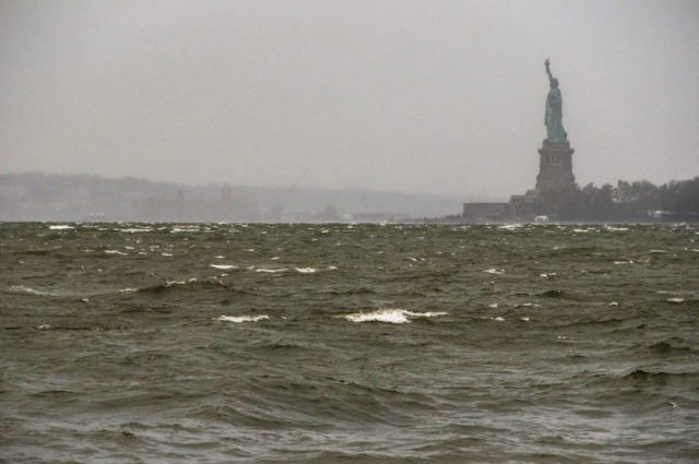 The Statue of Liberty stands tall amid choppy waters of the Hudson River, under an ominous gray sky.