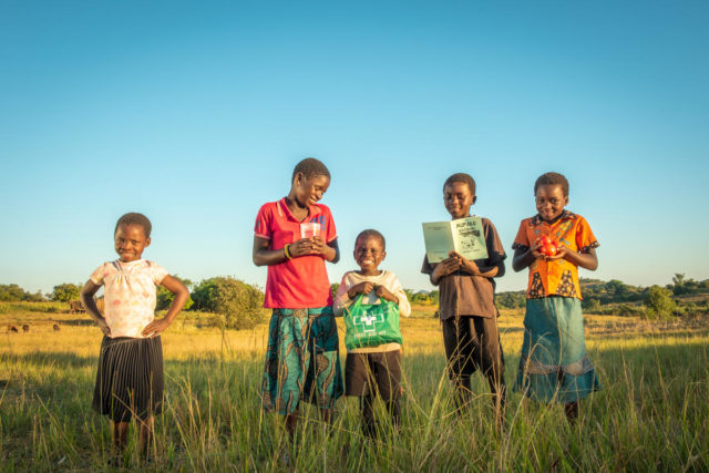 Five children smile in a field in Zambia.