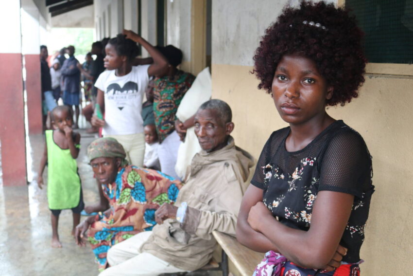 Sitting in a row of people at a shelter for people displaced by Cyclone Freddy in Mozambique, a young woman looks at the camera.