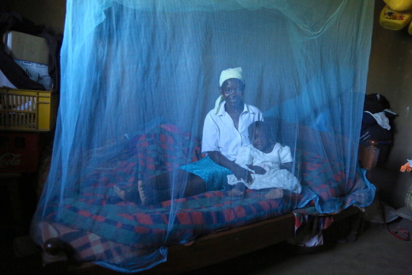 In Kenya, a mother and her baby sit under a blue bed net that protects them from malaria-carrying mosquitoes.