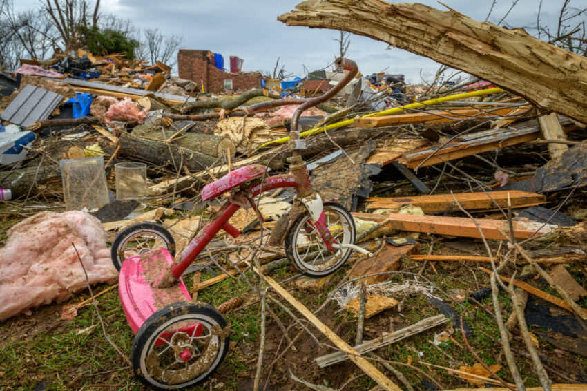 A lone red children's tricycle stands against a backdrop of debris following a destructive tornado.