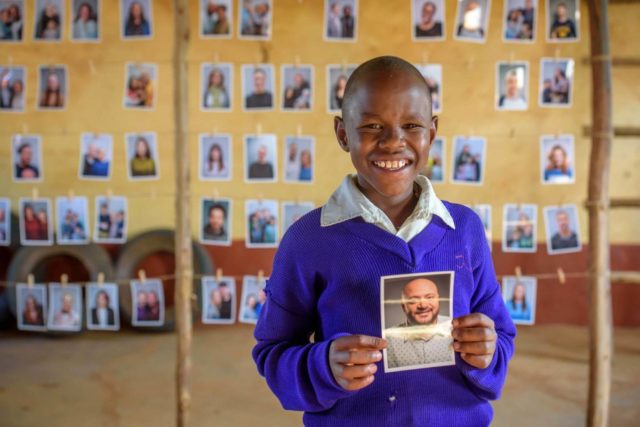 A boy in Kenya holds a photo of a man from Chicago he chose to be his sponsor.