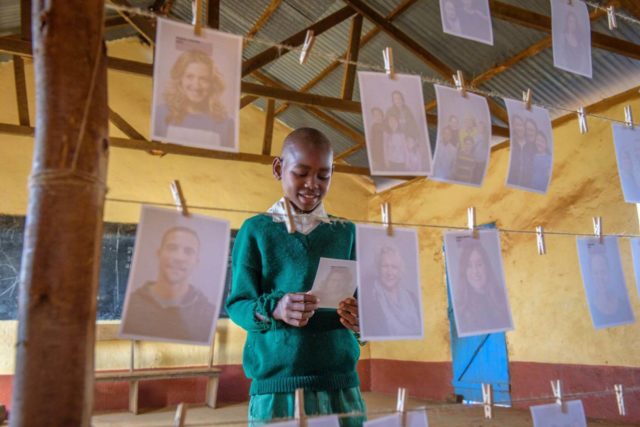A boy in Kenya chooses a photo of his sponsor off of a line strung with many photos of Americans.