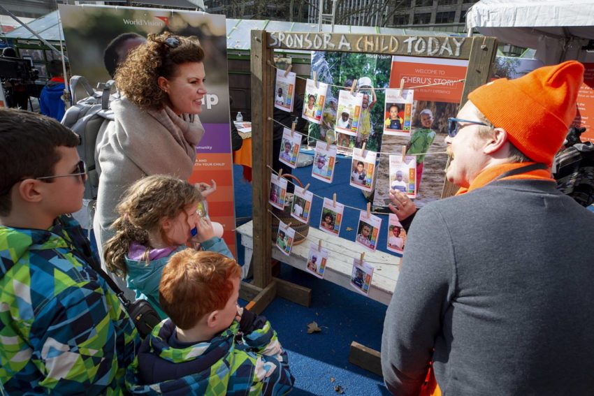 A mother and three children listen to someone in an orange hat talk at an activity station at an event in New York City.