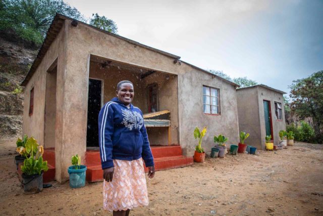 A woman stands in front of her house.