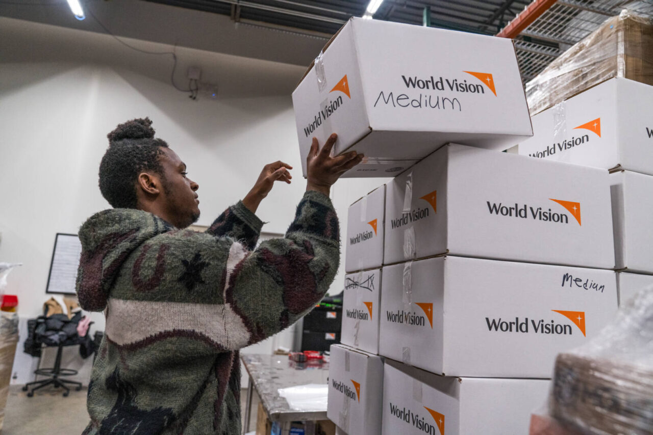 A young man adds a box to the top of a stack of boxes with World Vision logos.