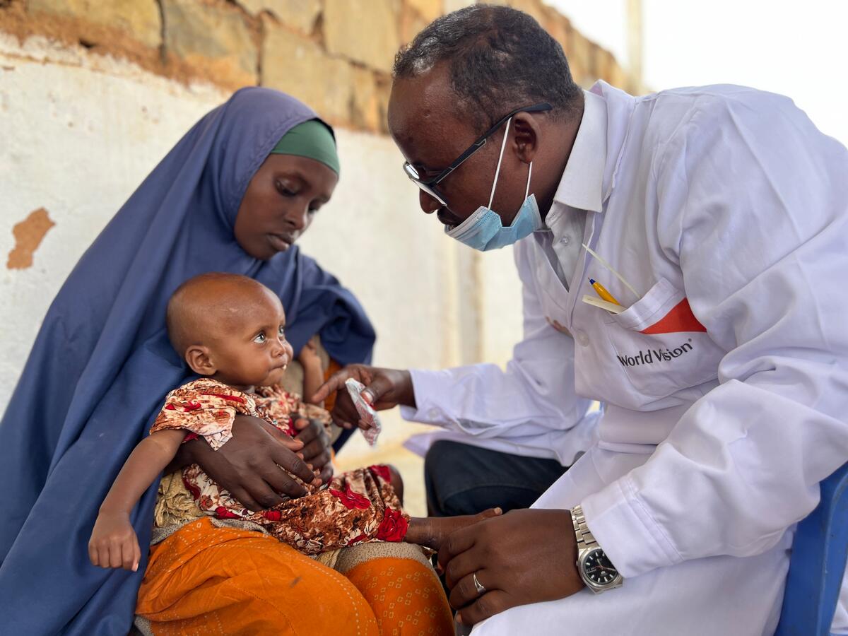 A healthcare provider in a World Vision lab coat gives baby a checkup as a mother holds her.