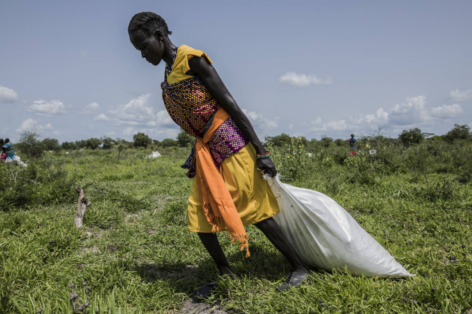 A woman wearing a yellow dress with a purple and orange sash pulls a bag of food supplies in South Sudan.