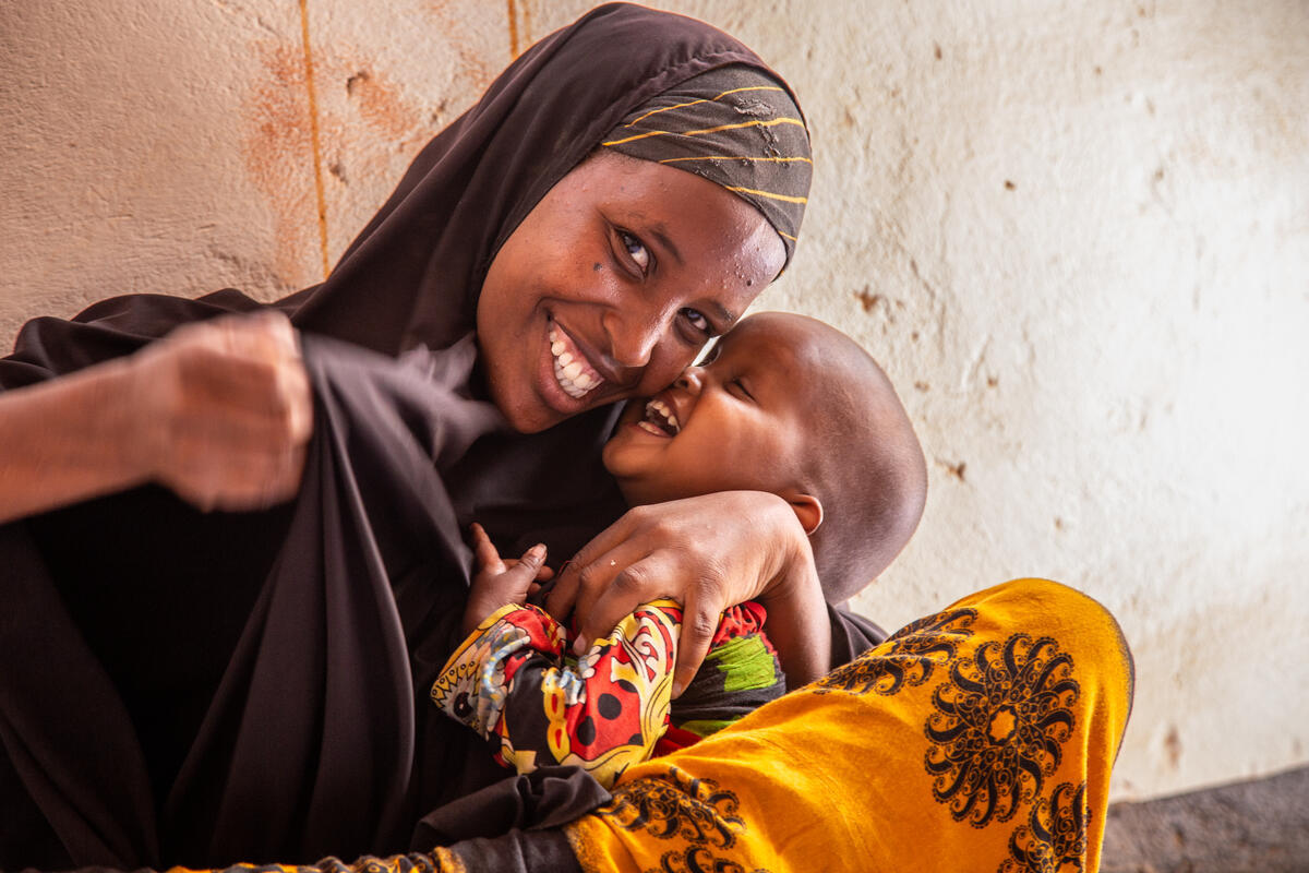 A woman in a black veil smiles brightly at the camera as her young child laughs in her embrace.