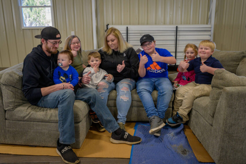 Six young kids and two adults give thumbs up and smiles from a new couch donated through World Vision.