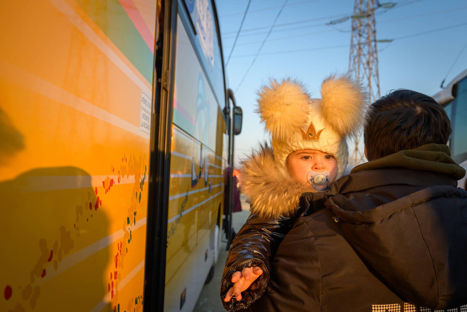 A child bundled against the cold is carried by an adult onto a bus, which is taking them away from the war in Ukraine.