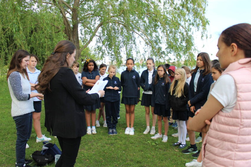 Elementary school students gather on a lawn for a discussion led by teachers and staff before their fundraising event.