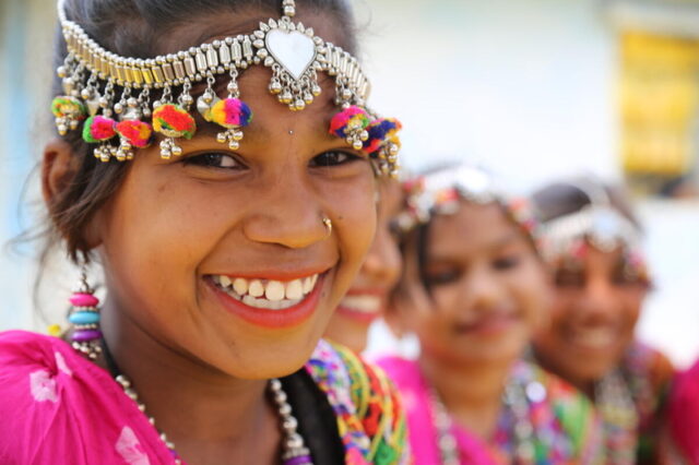A girl wearing a headband with colorful ornaments hanging from it smiles.