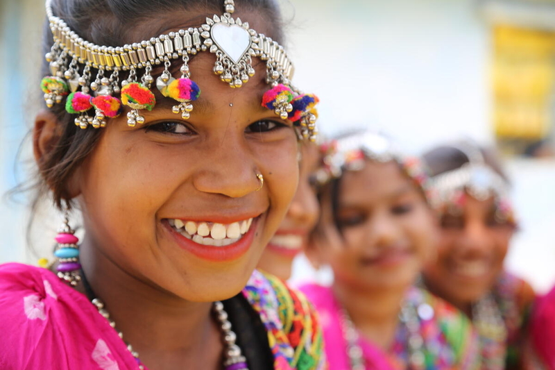A girl wearing a headband with colorful ornaments hanging from it smiles.
