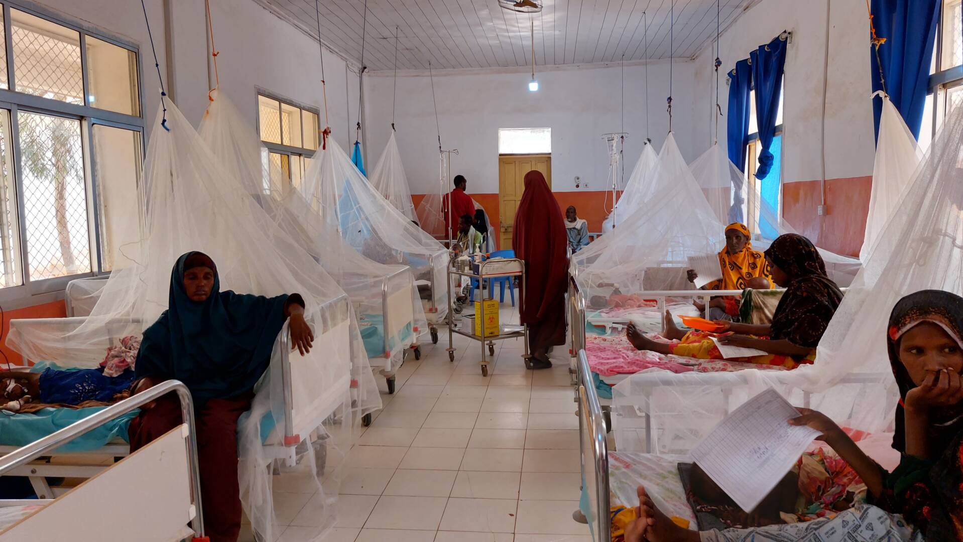 Inside a hospital in Somalia, malnourished children lie in beds, some covered by white fabric mesh tents.