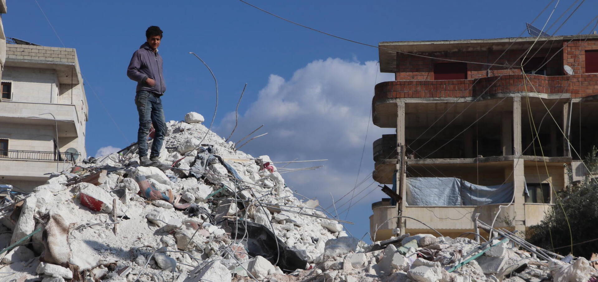 A young man stands atop a pile of rubble.