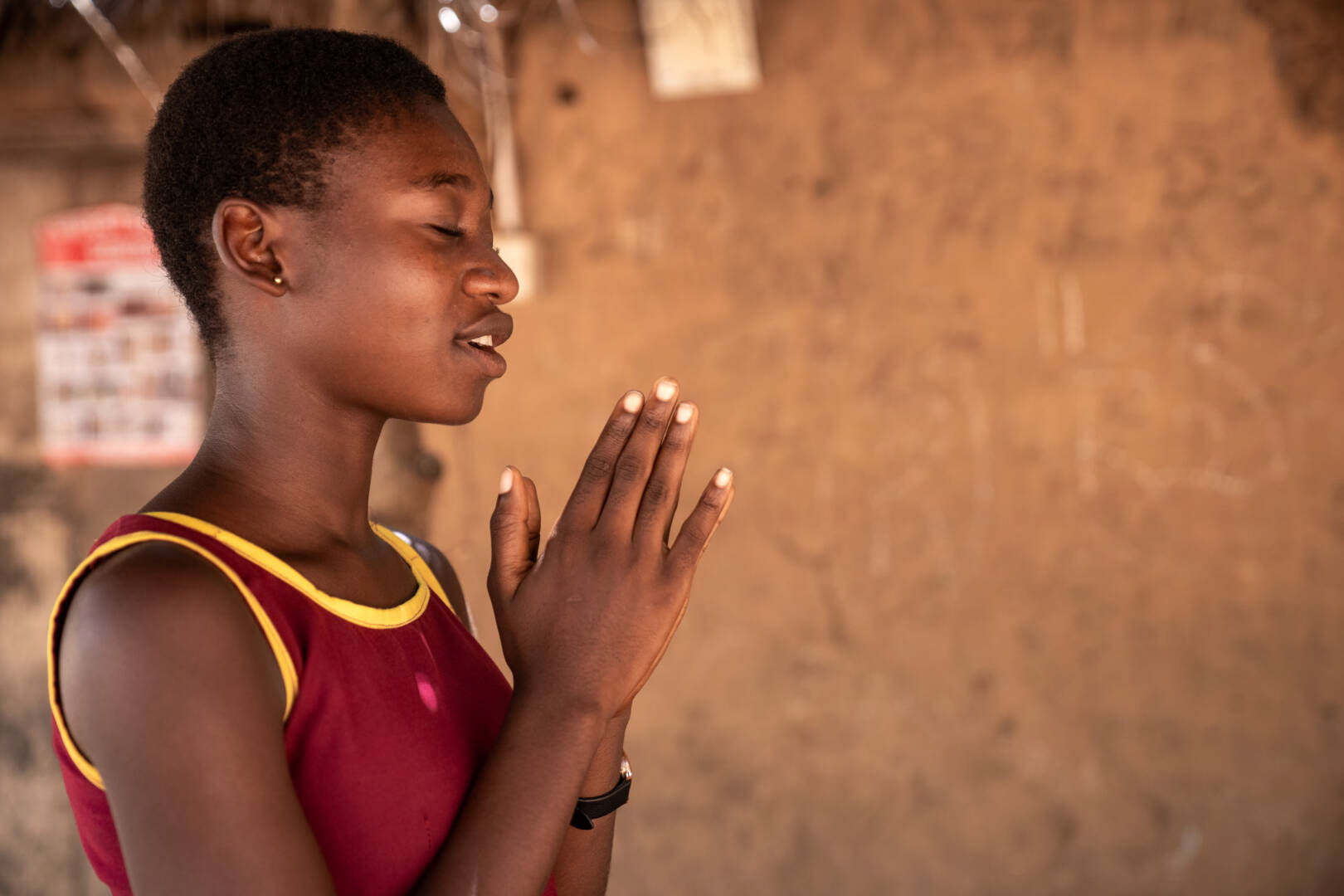 A teenage girl holds her hands together and closes her eyes in prayer.