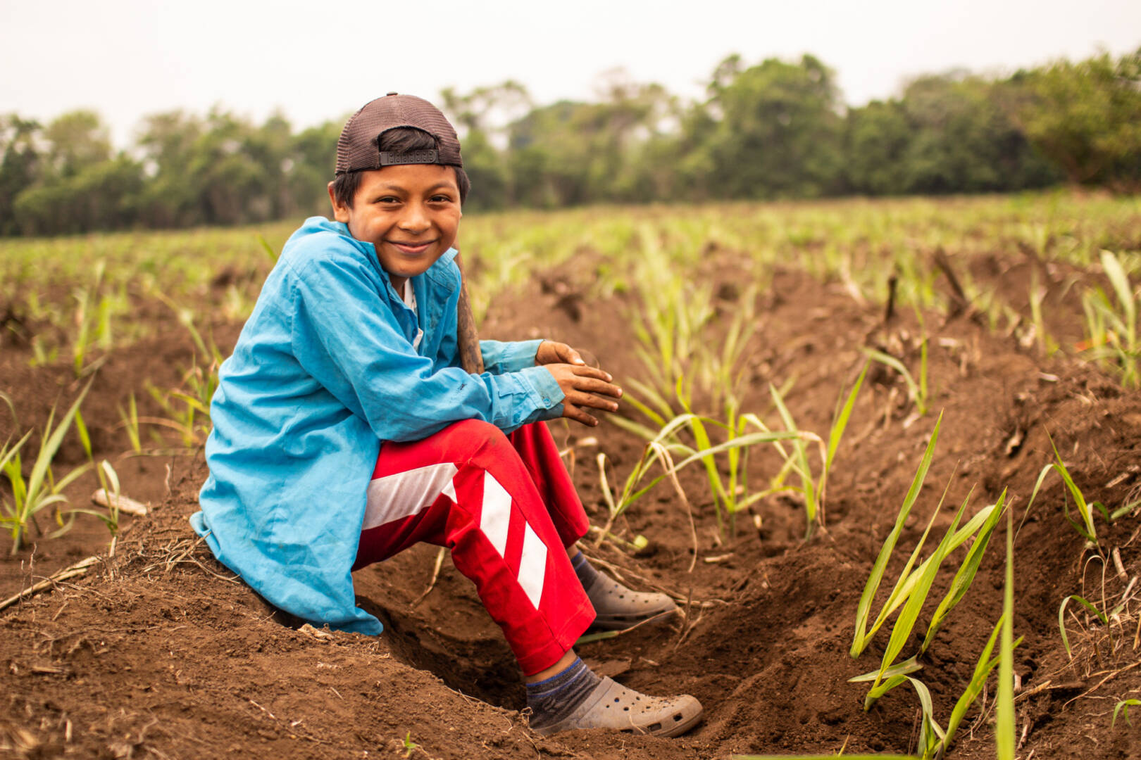A boy’s eyes glisten as he smiles while sitting in a field of growing crops.