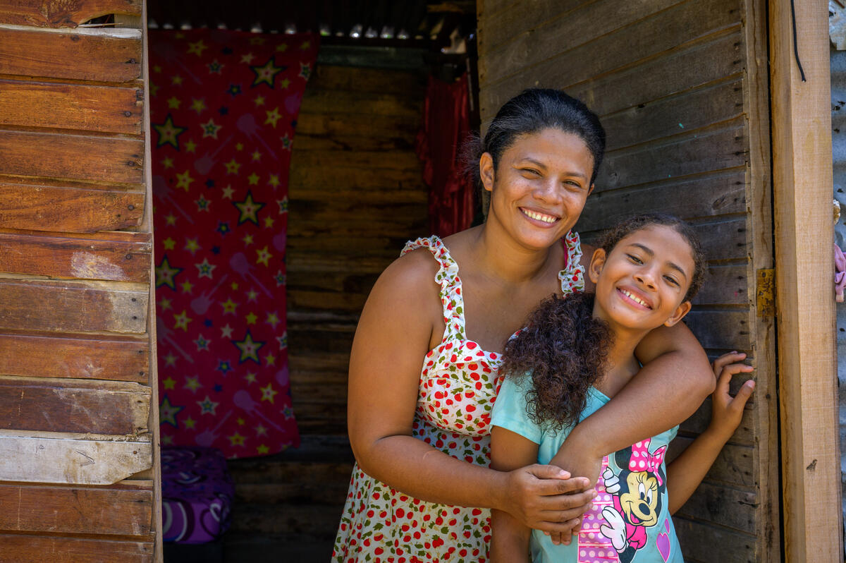 A woman with a bright smile hugs a girl in a Minnie Mouse T-shirt in the doorway of their home. 