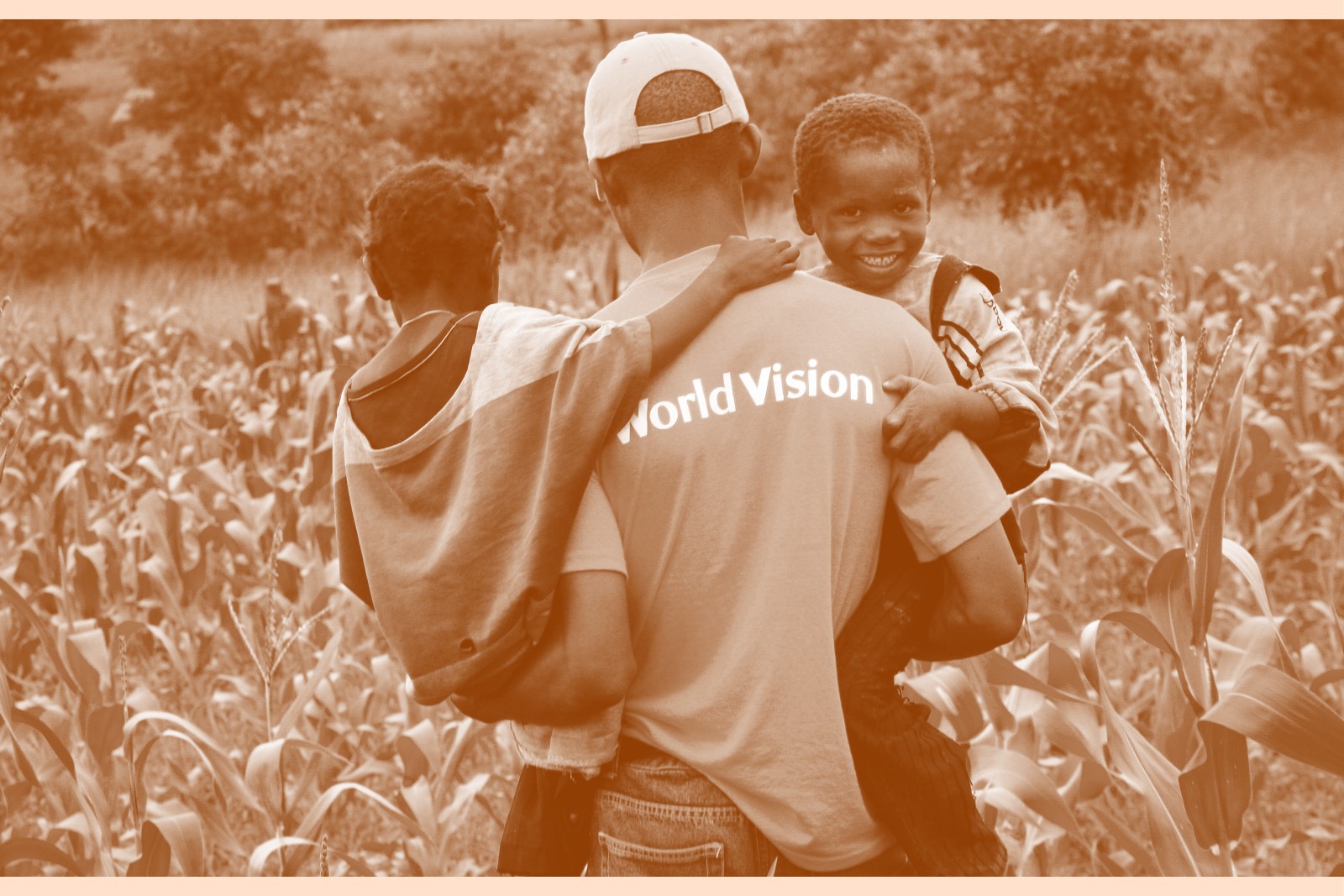 A man in a World Vision T-shirt holds two small children as he walks away from the camera.