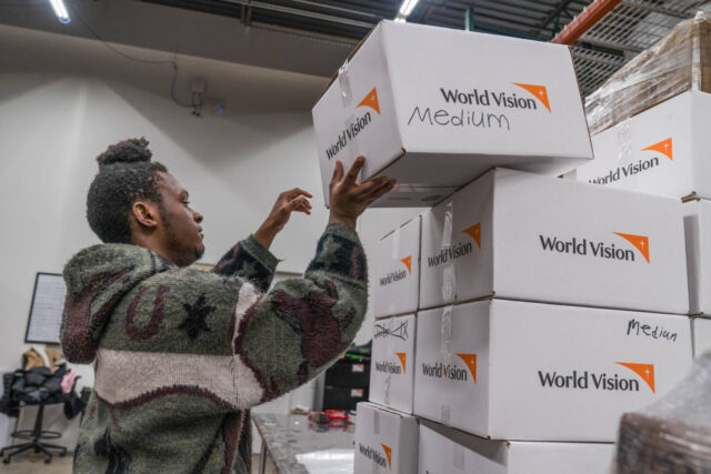 A young man places a box labeled with the World Vision logo onto a stack of similarly labeled boxes.