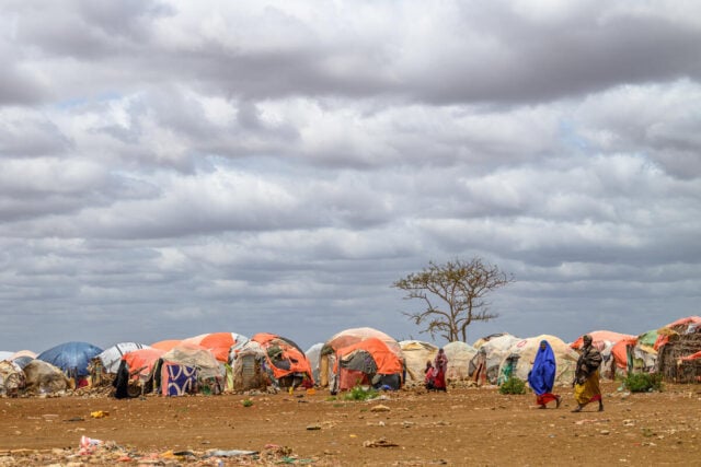 Two women pass in front of makeshift tents in a displacement camp.