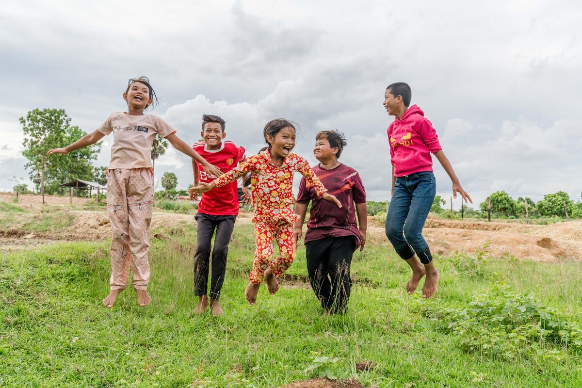 A group of children joyfully jumping in a green field.