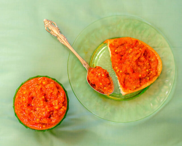 Photo of a red pepper spread in a bowl, on a spoon, and on a piece of bread.