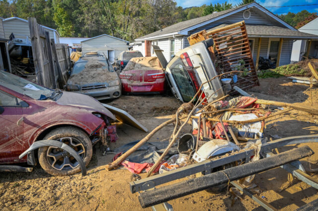 Overturned and damaged vehicles covered in mud and debris are seen on the front lawns of homes after a hurricane